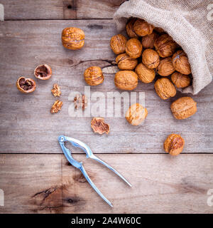 Walnuts kernels in hemp sack and whole walnuts on rustic old wooden background. Stock Photo