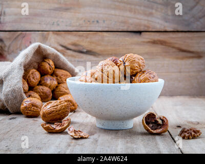 Walnuts kernels in hemp sack and whole walnuts on rustic old wooden background. Stock Photo
