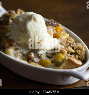 Close up shot of peach and pecan cobbler with a melting scoop of vanilla ice cream. Stock Photo