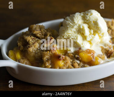 Close up shot of peach and pecan cobbler with a melting scoop of vanilla ice cream. Stock Photo
