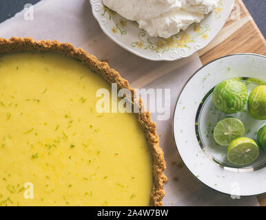 Homemade Key lime pie shown on parchment paper, shown with extra key limes and whipped cream. Stock Photo