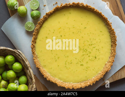 Homemade Key lime pie shown on parchment paper, shown with extra key limes. Stock Photo