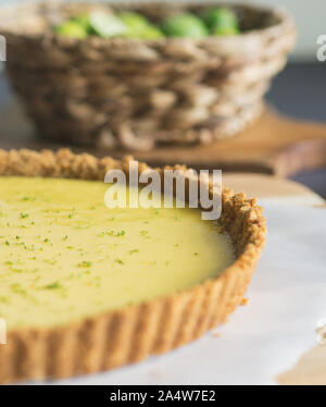 Homemade Key lime pie shown on parchment paper, shown with extra key limes. Stock Photo