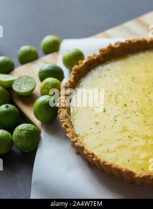 Homemade Key lime pie shown on parchment paper, shown with extra key limes. Stock Photo