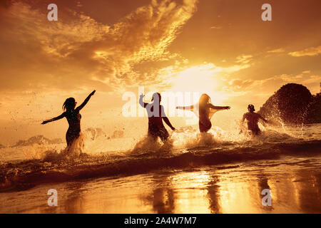 Four happy friends runs and having fun at beautiful sunset sea beach