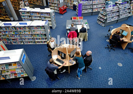 overview of library book shelves and people using computers Stock Photo