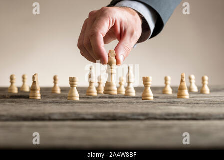 Businessman playing chess moving white king piece lifting it up in his fingers on an old wooden table. Stock Photo