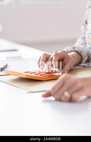 Female accountant or banker making calculations on orange manual calculator in the office. Stock Photo