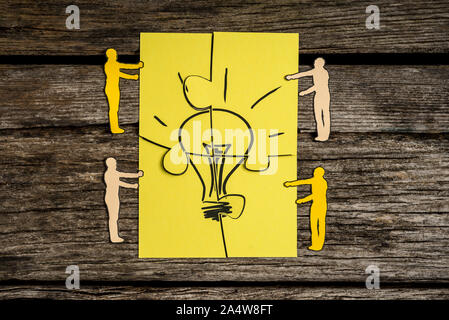 Four paper cutout silhouettes of men holding pieces of a jigsaw puzzle bearing the image of a light bulb to find the perfect idea. Stock Photo