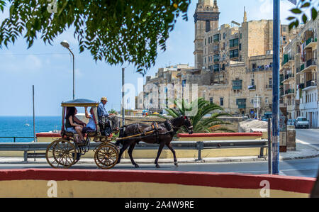 Valletta, Malta - August 30, 2019: Vintage horse carriage couching tourists along embankment street in Valletta in a summer sunny day. Stock Photo