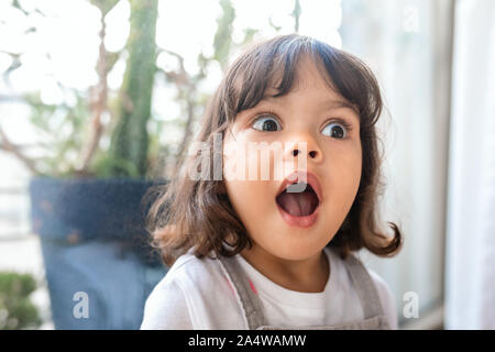Cute little girl looking surprised while playing at home Stock Photo