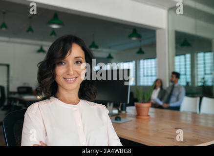 Smiling young businesswoman sitting by a table in an office Stock Photo