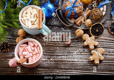 Flat lay Christmas background of two mugs of hot chocolate with marshmallows, spruce branch and tray with gingerbread man cookies on wooden table Stock Photo