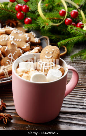 Pink mug with hot chocolate marshmallows and gingerbread man on background of spruce branch and tray with cookies Stock Photo