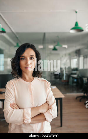 Smiling businesswoman standing with her arms crossed in an office Stock Photo
