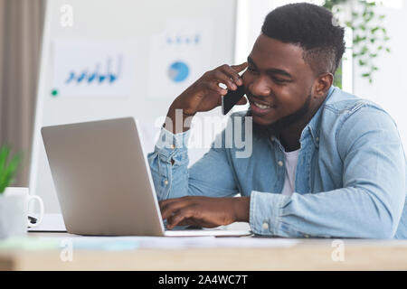 Employee talking on cellphone and working on laptop in office Stock Photo