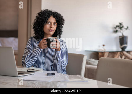 Female entrepreneur drinking coffee while working from home Stock Photo