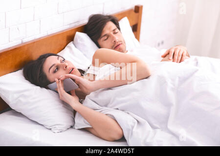 Cheating woman talking privately on cellphone in family bed Stock Photo