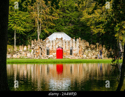 Quirky unusual rubble stone curling lodge reflected in artificial lake, Gosford Estate, East Lothian, Scotland, UK Stock Photo
