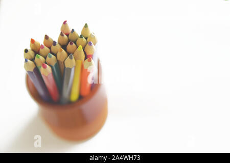 Colored pencils in a clay pot on a white wooden desk in an art lesson class. Empty copy space for Editor's content. Stock Photo