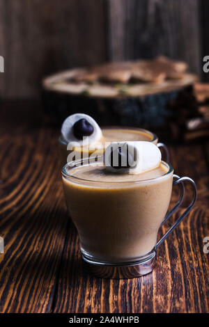 Happy  monster, pumpkin spice latte with whipped cream and big marshmallow eye on top, Halloween dessert, marshmallow smiley face on rustic wooden tab Stock Photo