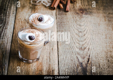 Happy  monster, pumpkin spice latte with whipped cream and big marshmallow eye on top, Halloween dessert in glasses Stock Photo