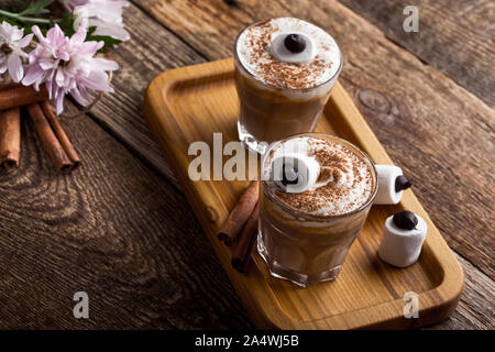 Happy  monster, pumpkin spice latte with whipped cream and big marshmallow eye on top, Halloween dessert in glasses Stock Photo