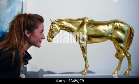 London, UK.  16 October 2019. A staff member views 'Racehorse - Gold' by Frippy Jameson at the preview of the Affordable Art Fair in Battersea. Celebrating its 20th anniversary, the show runs 17 to 20 October and features works of art from over 100 international galleries at prices ranging from GBP50 to GBP6,000.  Credit: Stephen Chung / Alamy Live News