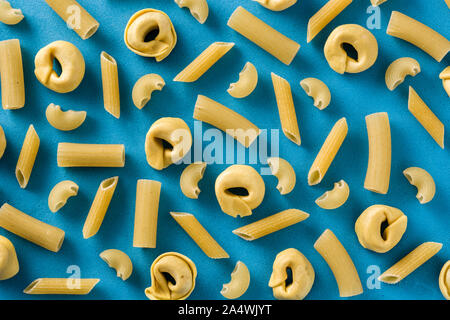 Different types of pasta pattern. Penne pasta and tortellini on blue background Stock Photo