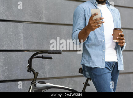 Unrecognizable man with bicycle using smartphone and drinking coffee outdoors Stock Photo