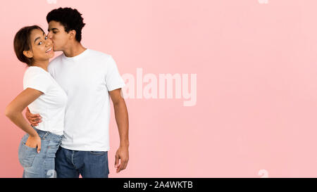 Afro guy kissing girlfriend in cheek, pink background