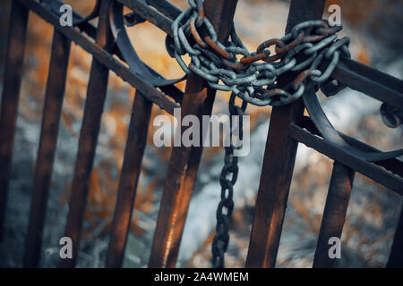 Gloomy rusty metal fence, which is closed on a metal long chain. Behind the fence is red grass and a path to the mystical land. Stock Photo