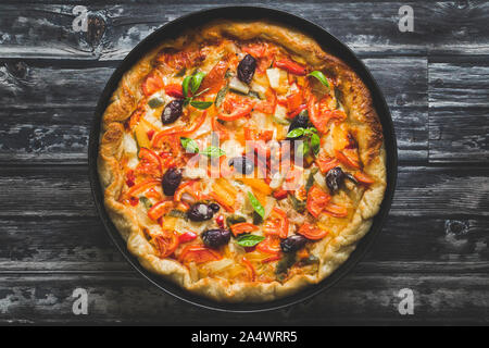 Homemade pizza with vegetables on a dark background. The pizza is viewed from above and is in a round baking tray, Copy space on the sides. Stock Photo