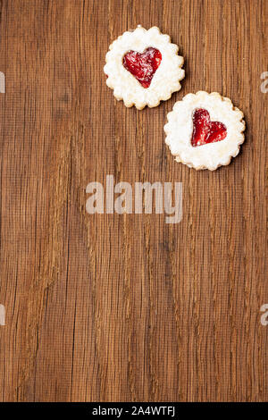 Two cookies filled with red jam with heart on wooden board Stock Photo