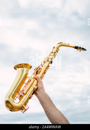 Hand Holding saxophone with cloudy and soft sky background. Music concept with copy space top. Stock Photo