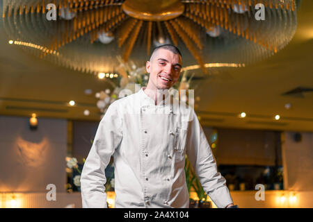 Young brutal handsome cook chief posing in modern luxury restaurant interior. Stock Photo