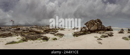panoramic of rocks on the beach where reflections are seen in puddles, moody skies with moody appearance Stock Photo