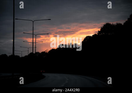 The autumn sun is setting behind a silhouette of trees next to the highway called Norra Ringen in the small city of Lund, Sweden. Stock Photo