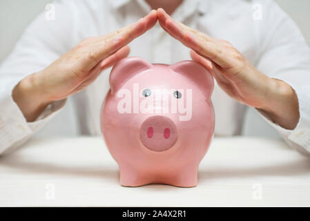 Hands protect the piggy bank. Concept for finance insurance, protection, safe investment or banking with hands over a piggy bank. Stock Photo