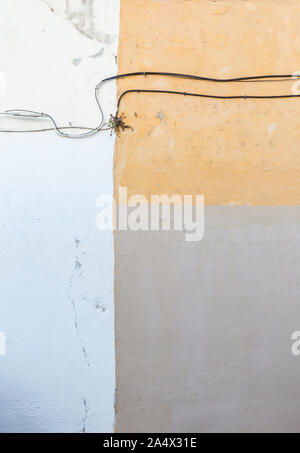 Full frame background of an old and weathered concrete wall with cables and painted in white, orange and beige. Stock Photo