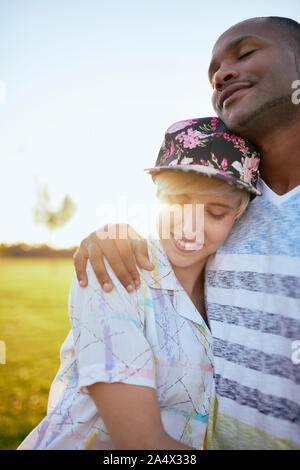 Mixed race couple of millennials in a grass field cuddling and s Stock Photo