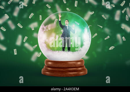 A tiny businessman inside a snowy crystal ball on a green background with dollar bills falling all around the place. Stock Photo