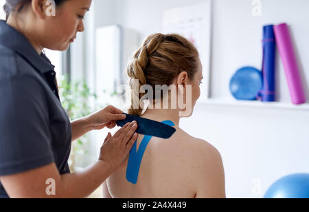 Chinese woman massage therapist applying kinesio tape to the sho Stock Photo