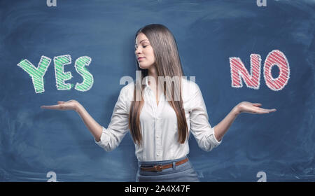 Beautiful businesswoman standing with open palms between big colorful words 'yes' and 'no' written on dark blue background. Stock Photo