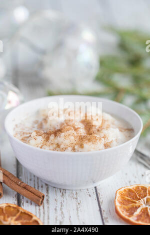 Close up of traditional rice pudding also known as tomtegröt or swedish risgrynsgröt. The rice pudding is in a white porcelain bowl on a white wooden Stock Photo