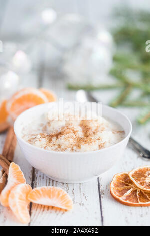 Traditional rice pudding also known as tomtegröt or swedish risgrynsgröt. The rice pudding is in a white porcelain bowl on a white wooden table, with Stock Photo