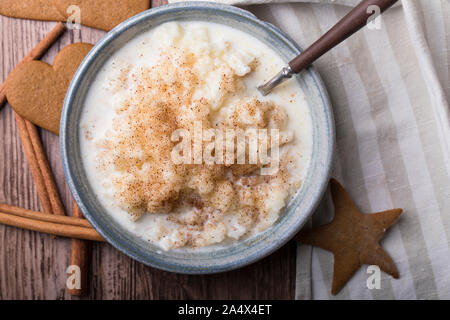 Traditional rice pudding also known as tomtegröt or swedish risgrynsgröt. The rice pudding is in a blue ceramic bowl on a wooden table, seen from abov Stock Photo