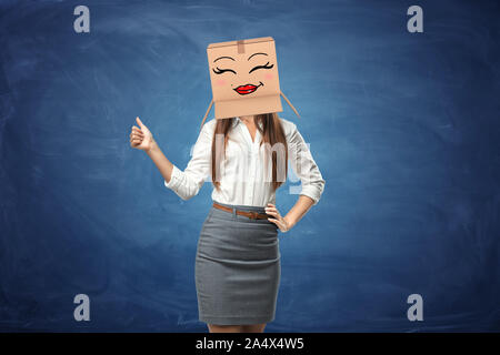 Young beautiful woman showing her thumb up and wearing cardboard box with drawn smiley face Stock Photo