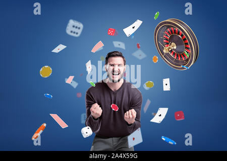 An emotional man cries angrily at camera, surrounded by a flying roulette, chips, cards and dice. Stock Photo