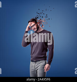 A young bearded man in glasses stands with his head on his forehead while several large pieces fly away from his head. Stock Photo